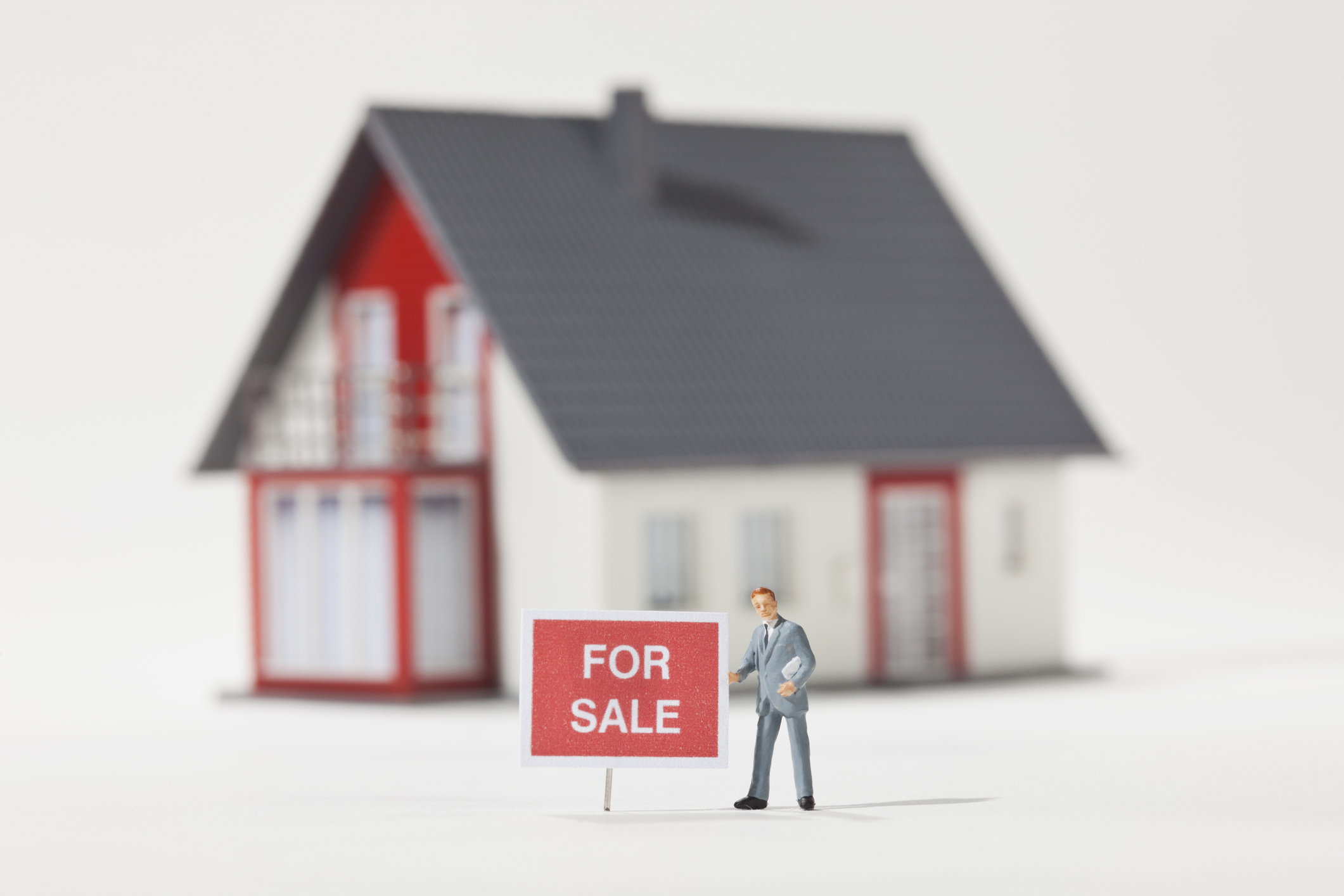 A miniature real estate agent figurine standing next to a FOR SALE sign